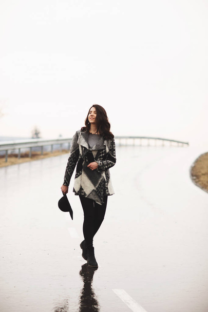 Girl with a black hat walking along the road on a rainy day - Фото, зображення
