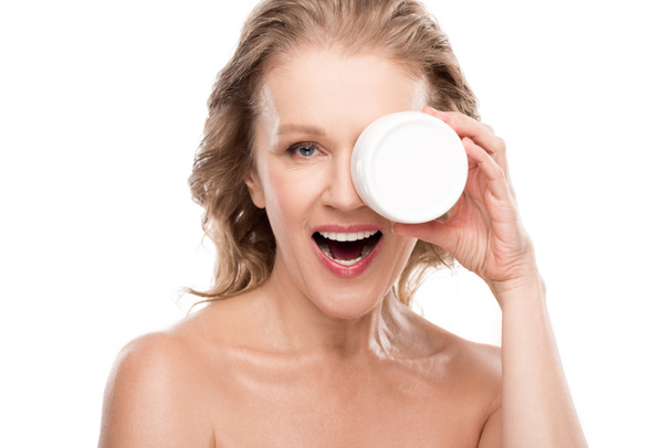 hermosa mujer madura sonriente sosteniendo contenedor con crema cosmética aislado en blanco
 - Foto, Imagen