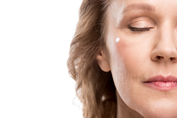 Vue recadrée de femme mature avec crème cosmétique sur le visage isolé sur blanc
 - Photo, image