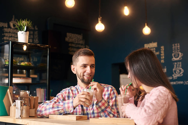 Młoda stylowa szczęśliwa para siedzi przy stoliku i pije kawę  - Zdjęcie, obraz