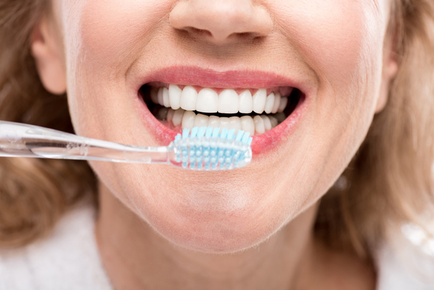 Bijgesneden weergave van middelbare leeftijd vrouw tanden poetsen, geïsoleerd op wit  - Foto, afbeelding