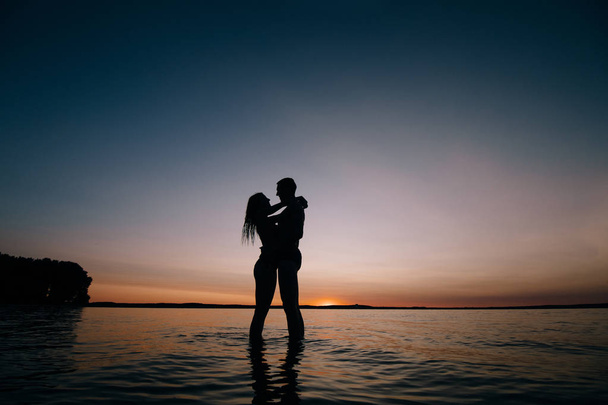 Pareja besándose en la playa con una hermosa puesta de sol en el fondo
 - Foto, Imagen