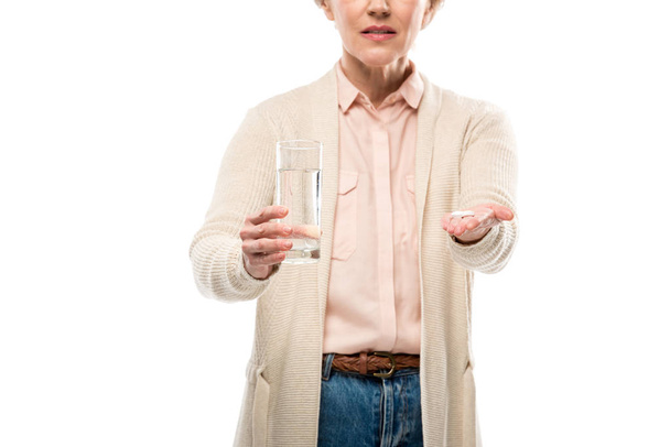 vista cortada de mulher de meia-idade com vidro de água e pílulas isolado em branco
 - Foto, Imagem