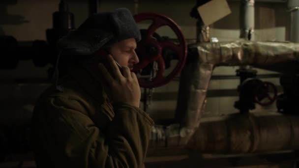 Homem russo de chapéu com abas auriculares, falando ao telefone em um porão escuro e decide assuntos de importância nacional
. - Filmagem, Vídeo