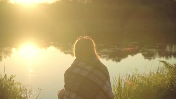 einsames Mädchen im Karo, das bei Sonnenuntergang am Ufer des Flusses sitzt. einsame Frau - Filmmaterial, Video