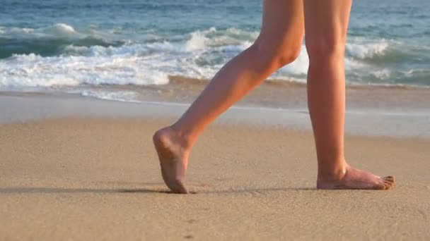 Pies femeninos caminando sobre arena dorada en la playa con olas oceánicas al fondo. Piernas de mujer joven pisando arena. Chica descalza en la orilla del mar. Vacaciones de verano. Cámara lenta Primer plano
 - Imágenes, Vídeo