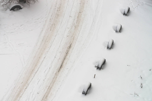 Snowy road. Fencing of old wheels. Fence from tires. Textured winter background. Abstract minimalist snowy weather texture. Car track in dirty snow. View from above. Traces of people and pets on snow. - 写真・画像