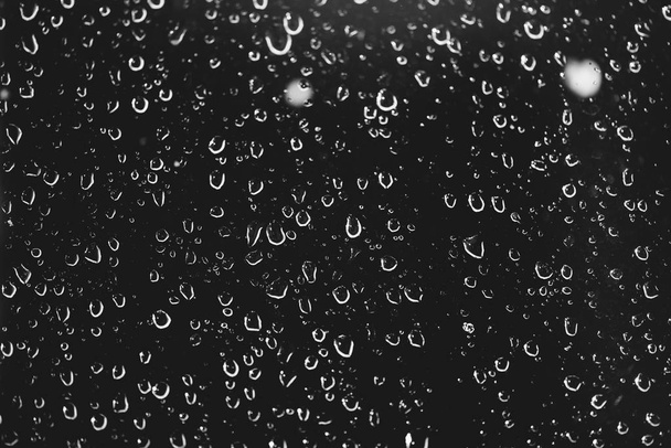 Špinavé sklo okna s kapkami deště. Barevné monochromatické tmavé pozadí s dešťové kapky. Kapičky a skvrny se blíží. Podrobná průhledná textura v makru s prostorem pro kopírování. Noční deštivé počasí. - Fotografie, Obrázek