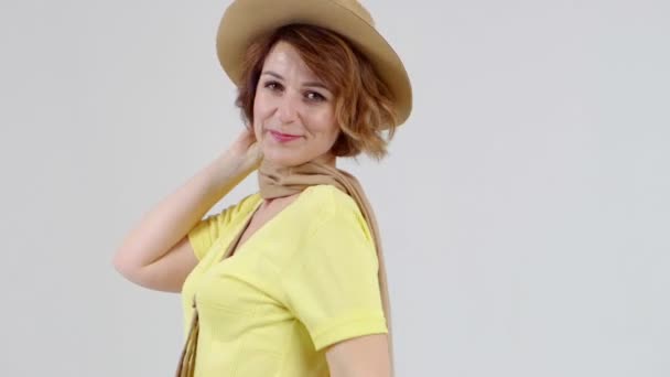 Jonge vrouw in gele blouse, beige hoed en sjaal poseert voor de camera op lichte achtergrond. - Video