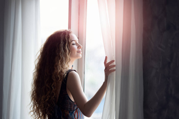 Jeune femme ouvrant le rideau le matin
 - Photo, image