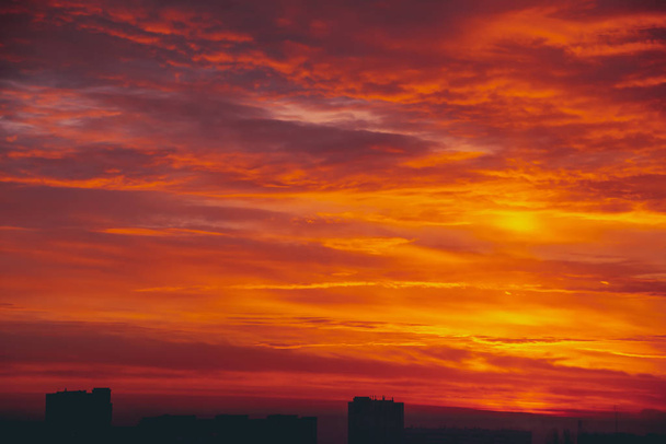 Αστικό τοπίο με έντονο φλογερό ξημέρωμα. Καταπληκτικό ζεστό δραματική συννεφιασμένο ουρανό πάνω από σκοτεινές σιλουέτες των κτίρια της πόλης. Πορτοκαλί φως του ήλιου. Ατμοσφαιρικό φόντο του sunrise νεφώσεις ο καιρός. Χώρο αντίγραφο. - Φωτογραφία, εικόνα