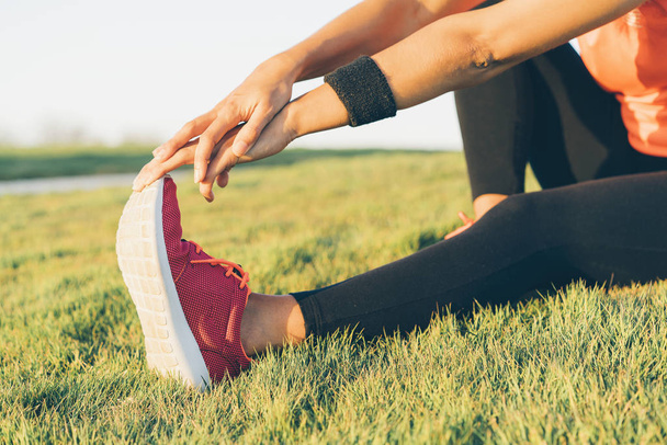 Mladá běžkyně si natahuje nohy, než běží do parku. Detailní atletické a zdravé dívka na sobě bílé a růžové tenisky. - Fotografie, Obrázek