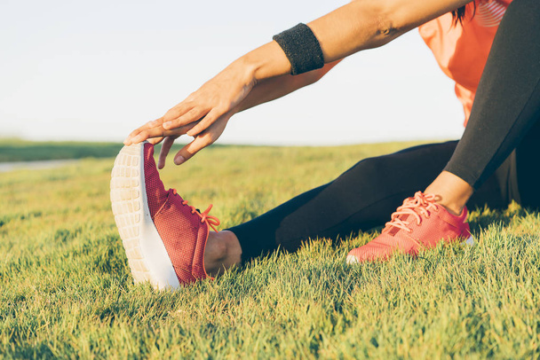 Jonge runner vrouw die benen strekt voordat ze in een park loopt. Close up atletisch en gezond meisje dragen witte en roze sneakers. - Foto, afbeelding