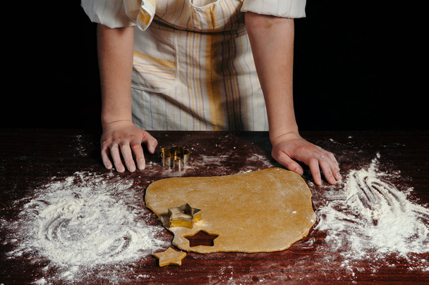 La muchacha en el delantal corta testo en forma de las galletas en forma de las estrellas sobre la mesa de madera. Primer plano
. - Foto, Imagen