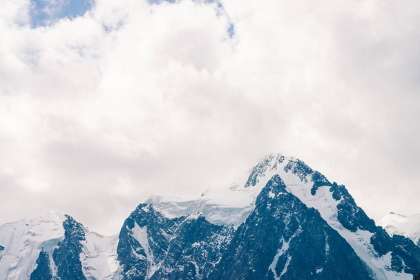 Geweldige enorme gletsjer top. Besneeuwde bergketen in overgegoten hemel. Prachtige gigantische rotsachtige heuvelrug met sneeuw in mist. Sfeervolle minimalistische landschap van majestueuze natuur van de Hooglanden. Rustige berglandschap. - Foto, afbeelding