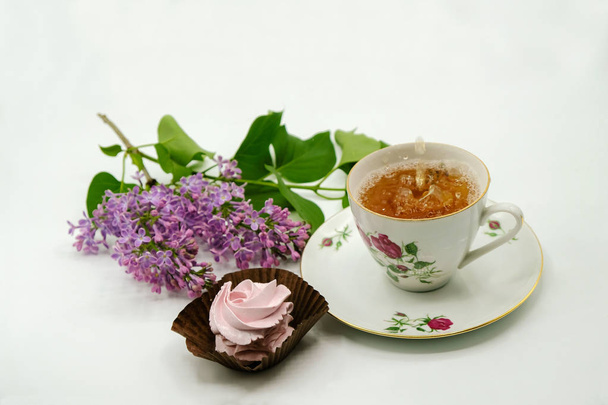 Tea egy porcelán csésze, rózsaszín fehérmályás, és virágok a lila lila, fehér felületen izolált. Térmásolat. Közelről. Képeslap. - Fotó, kép
