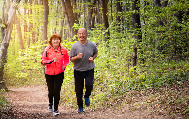 ハスバンフと妻はスポーツウェアを着て森の中を走っている - 写真・画像