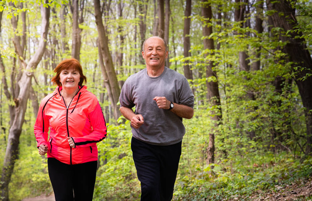 ハスバンフと妻はスポーツウェアを着て森の中を走っている - 写真・画像