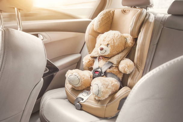 Carro de assento infantil. Um ursinho de pelúcia bege é preso com cintos de segurança em uma cadeira auto. Viajar de carro
 - Foto, Imagem
