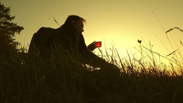 tourist drinks hot tea and watches sunset. lonely traveler sitting on top of a hill drinking coffee in thermos. rest after reaching goal. concept of freedom and dreams. world without borders - Photo, Image