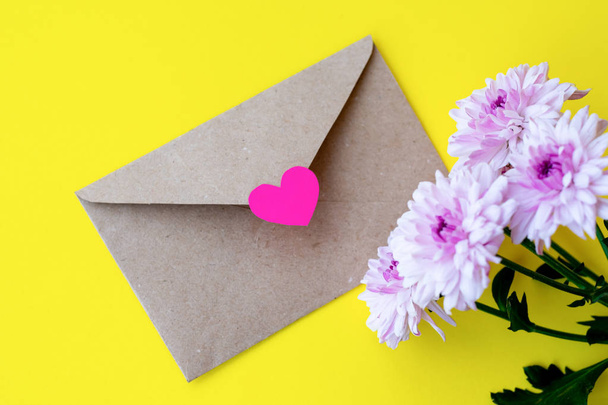 Love envelope with pink chrysanthemum flowers with pink heart on bright yellow bacground - Fotografie, Obrázek