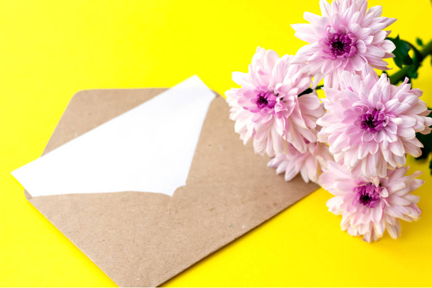 Love envelope with blank letter and pink chrysanthemum flowers on bright yellow bacground. Copy space - Fotoğraf, Görsel