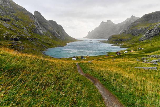 Túraútvonal vezet egy gyönyörű öbölben körülvett hegyek és egy kis falu közelében Bunes strand és Vinstad a Lofoten szigeteken Norvégiában - Fotó, kép