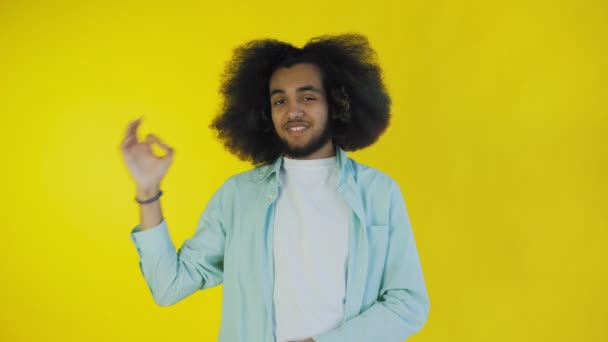 Uśmiechnięty, atrakcyjny afro-amerykański facet pokazujący ok gest stojąc odizolowany na żółtym tle. Pojęcie emocji - Materiał filmowy, wideo