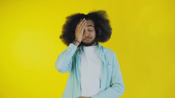 Disappointed afro american male doing facepalm gesture against yellow background. Concept of emotions - Séquence, vidéo