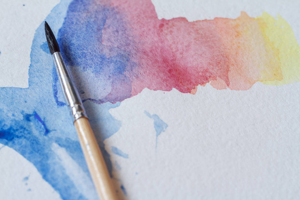 Close-up van prachtige aquarel penseelstreken op een wit blad, een penseel in de afbeelding - Foto, afbeelding