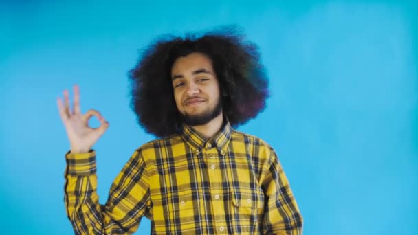 Mosolygó vonzó afro-amerikai srác mutatja az OK gesztust, miközben állva elszigetelt kék háttérben. Az érzelmek fogalma - Felvétel, videó