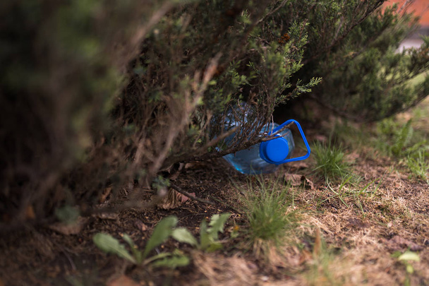 Botella plástica azul grande tirada en el suelo en un árbol en un bosque de parque - Tirada no reciclada - Basura y contaminación de la ciudad y la naturaleza - Basura decaída
 - Foto, Imagen