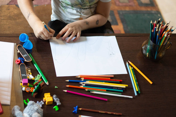 子供の手が木製のテーブルに紙の白いシートに色鉛筆で描かれています。. - 写真・画像