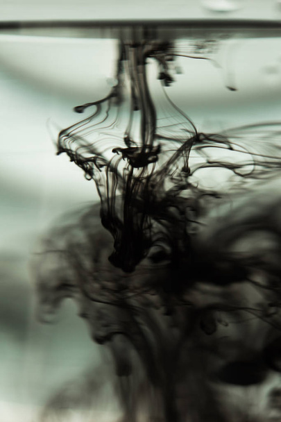 a cloud of ink in a transparent glass cup with clear water against the backdrop of a striped screen with rays of light. Template, layout, background, texture. macro diffusion black and white - Foto, imagen