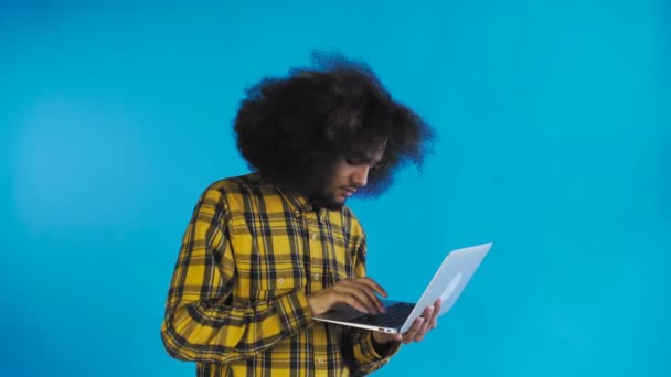 Hombre afroamericano feliz usando portátil sobre fondo azul. Concepto de emociones
 - Imágenes, Vídeo