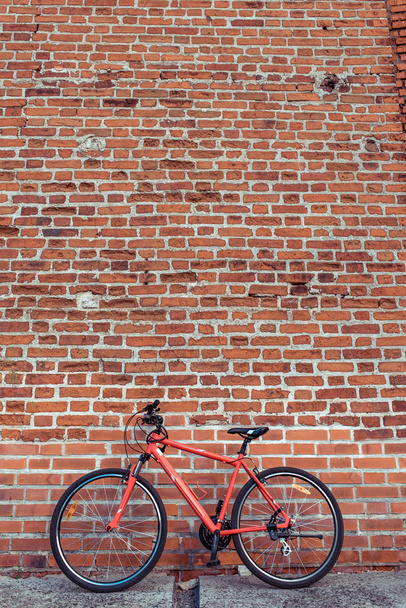 Red bicycle on the background of a brick old wall. Free space for text. The concept of parking and abandoned bike. Locked and parked, locking cable on the frame of the bike. In summer in the city. - Valokuva, kuva