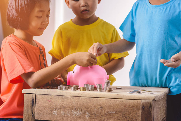 Группа азиатских детей помогает положить монеты в свиной запрет
 - Фото, изображение