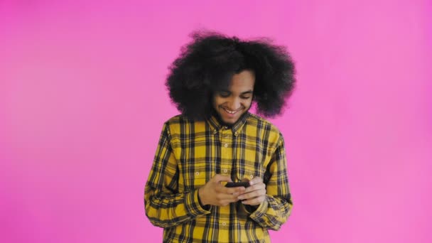 Portrait of African American man with curly hair chatting on smartphone on purple background. Concept of emotions - Footage, Video