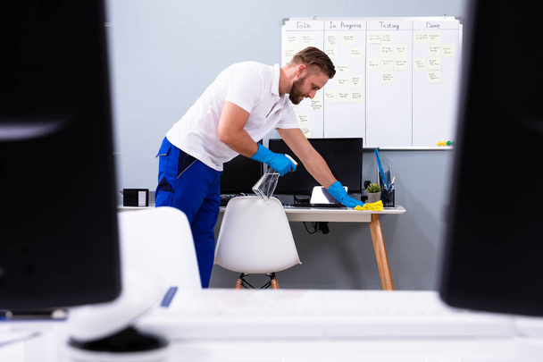 Hausmeister putzt weißen Schreibtisch in modernem Büro - Foto, Bild