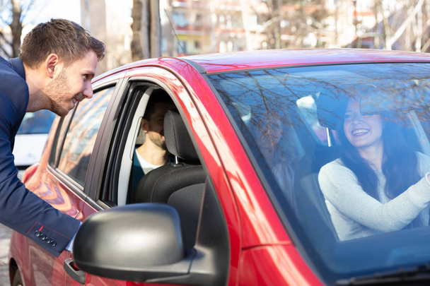 Sorrindo jovem falando com uma senhora sentada dentro do carro
 - Foto, Imagem