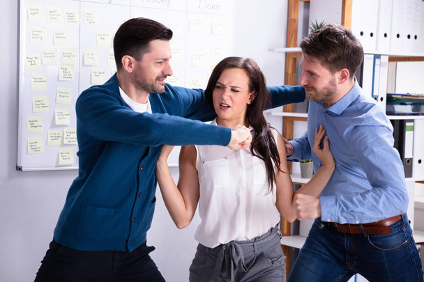 Close-up Of Businessmen Getting Into A Fight Woman Trying To Separate Them In Office - 写真・画像