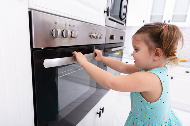 kleines Mädchen spielt mit elektrischer Mikrowelle in der Küche - Foto, Bild