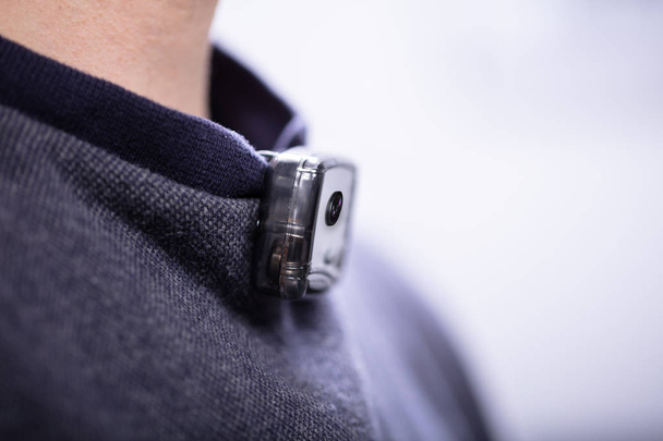 Close-up Of Surveillance Camera On Man's T-shirt Near His Neck - Foto, Bild