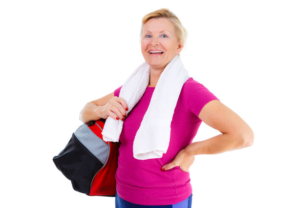 Συνταξιούχος γυναίκα άθλημα. Χαρούμενος από γηραιότερος ηλικιωμένη κυρία με αθλητική τσάντα στον ώμο και πετσέτα γύρω από το λαιμό στο αθλητικό ντύσιμο μετά την άσκηση Fitness στο γυμναστήριο κρατώντας, απομονωμένα σε λευκό, θετικά συναισθήματα - Φωτογραφία, εικόνα