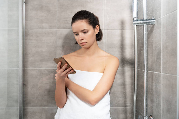pensive young woman in towel using smartphone in bathroom - Foto, Imagem