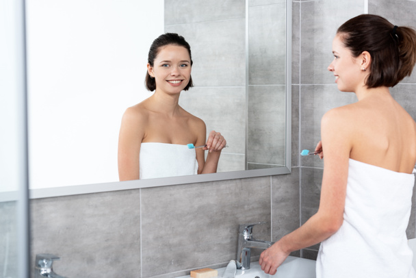 pretty smiling girl holding toothbrush near mirror in bathroom - Photo, Image