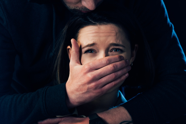částečný pohled na zločince útočící na vyděšený ženský a zakrývající její ústa izolovaná na černém - Fotografie, Obrázek