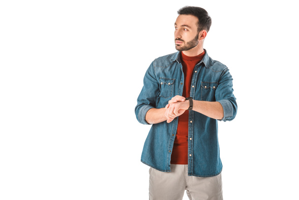 serious man in denim shirts looking away and touching watch isolated on white - Foto, imagen