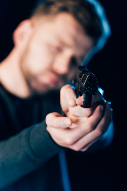 selective focus of criminal aiming gun at camera isolated on black - Foto, afbeelding