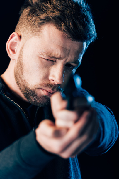 bearded criminal aiming gun at camera isolated on black - Foto, afbeelding